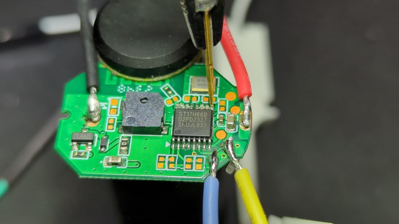 Small BLE control board under a probe tip, with wires soldered to test pads and the BLE SoC exposed