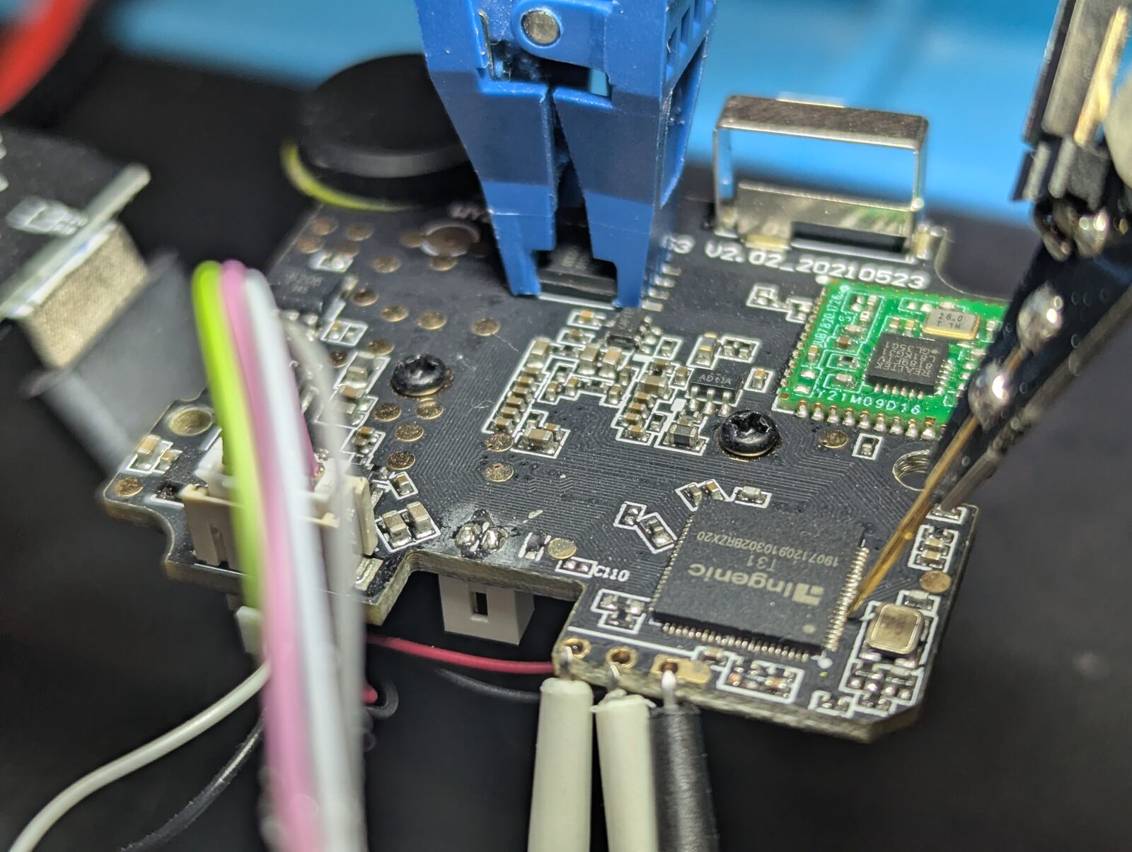 A blue SOIC-8 test clip attached to the flash chip on the camera board, with ribbon and jumper wires running off to a programmer, the Ingenic T31 visible nearby.